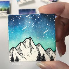 a hand holding up a small card with mountains and stars in the sky on it