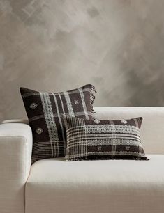 two black and white pillows sitting on top of a couch next to a gray wall