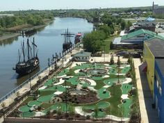 an aerial view of a miniature golf course next to a river with a ship in the background