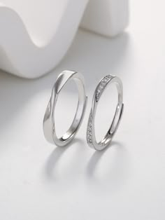 two silver rings sitting next to each other on a white table with a vase in the background