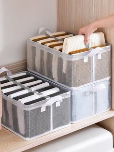 two storage bins with dividers and handles on top of a wooden shelf next to a toilet paper dispenser