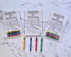 three coloring books with markers and crayons next to them on a marble surface