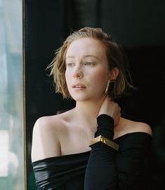 a woman in black is looking out the window with her hand on her shoulder and wearing gold earrings