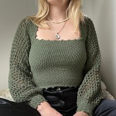 a woman is sitting on a bed wearing a green sweater and black pants with her hands in her pockets