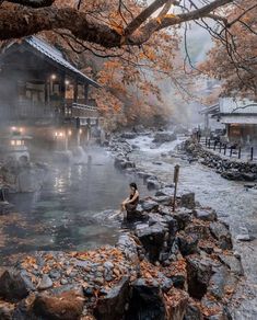 a woman sitting on rocks in the middle of a river with steam rising from it