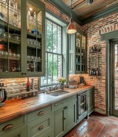 a kitchen with green cabinets and wooden counter tops next to a brick wall that has glass doors