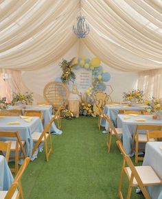 a room filled with lots of tables covered in blue and yellow tablecloths under a white tent