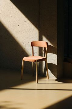 a chair sitting in front of a concrete wall with the sun shining on it's side