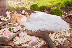 a woman in a white wedding dress laying on the ground surrounded by flowers and branches