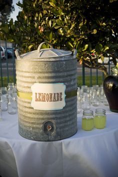 a large metal barrel sitting on top of a white table covered in lemonade bottles