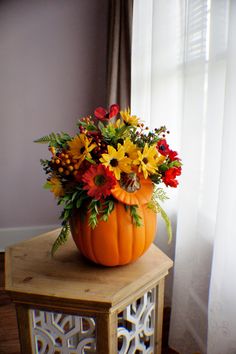 a pumpkin filled with flowers sitting on top of a wooden table next to a window