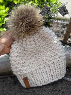 a hand holding a white knitted hat with a brown pom - pom