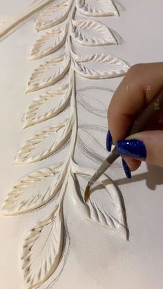 a woman is using scissors to paint the leaves on a piece of white paper that has been carved into it