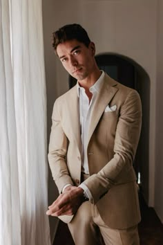 a man in a tan suit standing next to a window