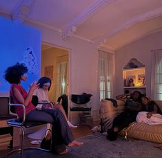 three women sitting on couches in a living room watching something on the tv screen