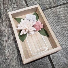 some paper flowers in a glass jar on a wooden tray with wood plank flooring