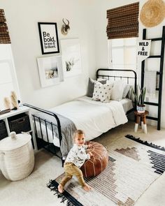 a toddler sitting on the floor in a bedroom with white walls and rugs