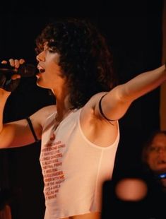 an image of a woman singing on stage with her arms out to the side while holding a microphone