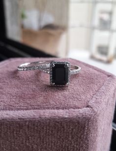 a black diamond ring sitting on top of a purple velvet box in front of a window