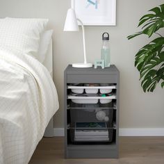 a white night stand next to a bed with a plant on the side and an art piece hanging above it