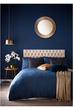 a bed with blue sheets and pillows in front of a round mirror on the wall