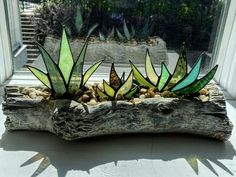 three green glass plants sitting on top of a piece of driftwood in front of a window