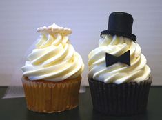 two cupcakes with white frosting and a black top hat on each one