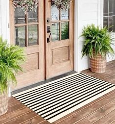 two potted plants sitting on the front porch next to an entryway rug with black and white stripes