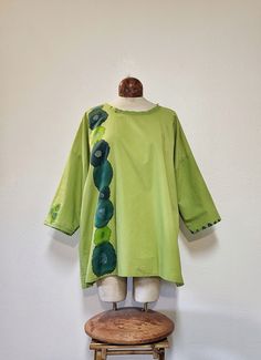 This tunic style top was made from a spring green 100% cotton sheet. It has handpainted happy flowers on it in shades of turquoise, teal and granny apple green. There's handstitchrd detail around the neckline and one of the sleeves. This top is super lightweight so it would be perfect for a hot summer day. She's a one size fits most.  The model generally wears a medium and is 5'9.  It would be oversized on a small and medium frame and fit nicely on a large. Handwashing or a delicate machine wash is recommended. Please let me know if you have any questions. Thank you! Green Lagenlook Long Sleeve Blouse, Relaxed Fit Blouse With Natural Dye For Spring, Oversized Green Bohemian Tunic, Green Relaxed Fit Tunic For Summer, Green Casual Relaxed Fit Tunic, Green Relaxed Fit Casual Tunic, Spring Green Lagenlook Tops, Green Tunic Tops For Spring, Oversized Green Cotton Blouse