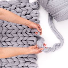 two hands holding yarn on top of a gray blanket and ball of yarn in the background