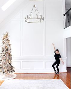 a woman standing in front of a christmas tree with her arms up and one hand on the wall