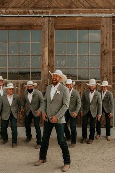 a group of men standing next to each other in front of a wooden building wearing cowboy hats