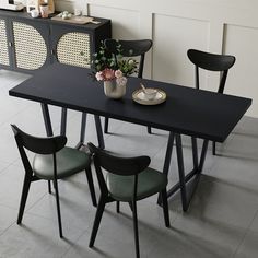 a black table with four chairs and a vase filled with flowers sitting on top of it