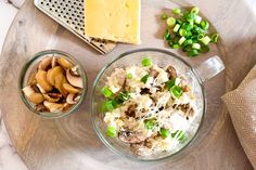 two bowls filled with food sitting on top of a wooden table next to cheese and green onions