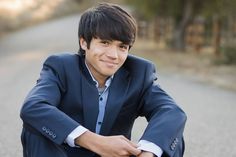 a young man in a blue suit sitting on the ground with his arms folded out