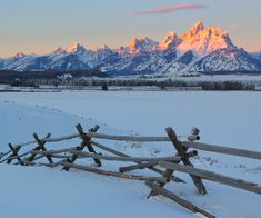 a wooden fence in the snow with mountains in the backgroung and clouds in the sky