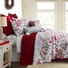 a bed with red and white comforters in a bedroom next to a window,