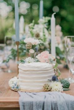 a white wedding cake sitting on top of a wooden table next to candles and flowers