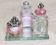 three perfume bottles sitting on top of a glass tray next to each other, one pink and one white