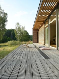 a wooden deck with two chairs on it next to a sliding glass door and trees