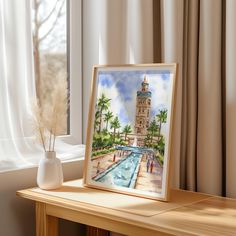 a painting on a table next to a window with a view of a fountain and palm trees