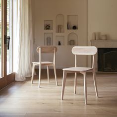 two wooden chairs sitting next to each other on top of a hard wood floor in front of a fireplace