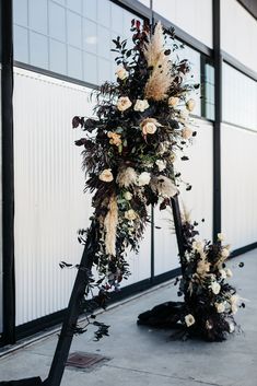 a tall floral arrangement on the side of a building with white flowers and feathers hanging from it's poles