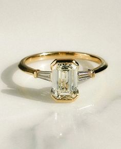 an emerald and baguette diamond ring with three tapers on the band, set in yellow gold