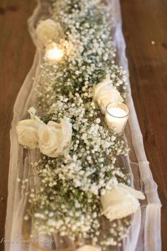 flowers and candles are arranged on a long stretch of clear glass with white petals, baby's breath