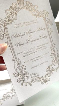 a person holding up a wedding card with an ornate frame on it's front