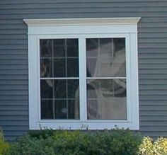 a dog looking out the window of a house with bushes and shrubs in front of it