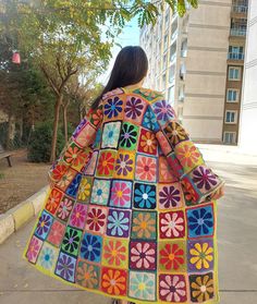 a woman is walking down the sidewalk wearing a colorful crocheted jacket with flowers on it