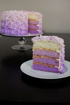 a slice of cake with purple frosting sitting on a plate next to the rest of the cake