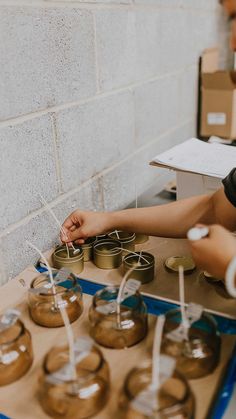 two people reaching for jars with candles in them on a table next to some boxes